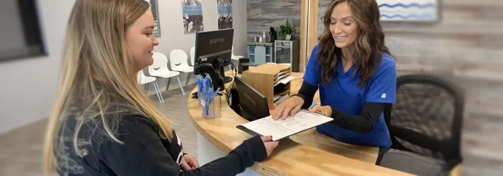 A professional setting where a staff member assists a visitor with paperwork at the reception desk.