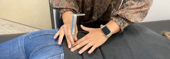 Close-up of a practitioner applying a torque release instrument to the patient’s lower back during a chiropractic adjustment.